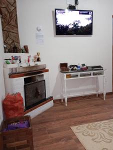 a living room with a fireplace and a tv on the wall at Casa de Campo Refúgio Jaguary in Monte Verde