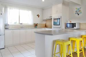 a kitchen with white cabinets and yellow bar stools at Allara 1 in Merimbula +6 photos