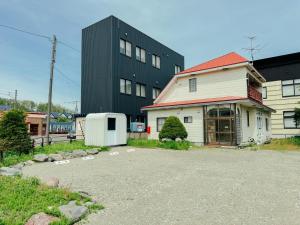 a house with a building in the background at ゲストハウスVACILANDO in Chitose