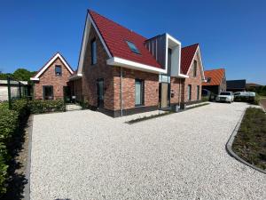 Una casa de ladrillo con techo rojo en un camino de entrada. en Vakantiewoning Westkaap, en Westkapelle