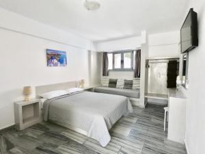 a white bedroom with a bed and a flat screen tv at Anny Studios & Rooms Perissa Beach in Perissa