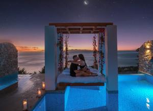 a couple sitting on a bed with a view of the ocean at Emerald Villas & Suites - The Finest Hotels Of The World in Agios Nikolaos