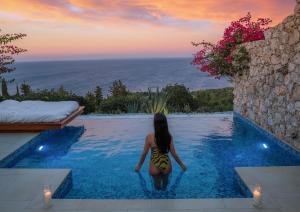 a woman in a swimming pool looking at the sunset at Emerald Villas & Suites - The Finest Hotels Of The World in Agios Nikolaos