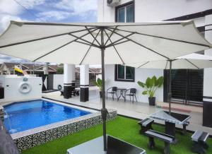 a pool with an umbrella next to a house at Saujana Homestay Perak in Seri Iskandar