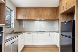 a kitchen with white cabinets and a black refrigerator at Ventura Delight Townhouse with Parking and Patio in Auckland