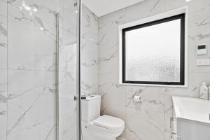 a white bathroom with a toilet and a window at Ventura Delight Townhouse with Parking and Patio in Auckland +11 photos
