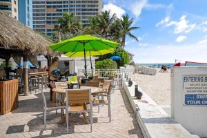 eine Frau steht mit einem grünen Sonnenschirm an einem Tisch am Strand in der Unterkunft Relaxing Escape Oceanfront Pool Gem On The Beach in Fort Lauderdale
