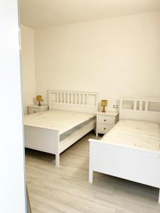 Casa Giannina a Marina di Cecina by Zoom In Earth في مارينا دي سيسينا: سريرين في غرفة نوم بجدران بيضاء وأرضية خشبية