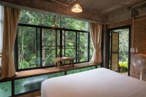a bedroom with a bed and large windows at Bee Forest in Ban Pok Nai