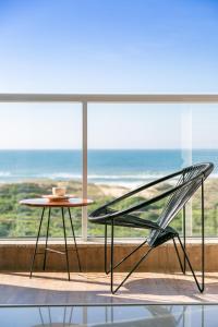 uma cadeira e uma mesa em frente a uma grande janela em Apartamento Vista Mar no Novo Campeche em Florianópolis