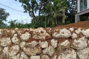 a stone retaining wall next to a house at La Maison du haut! in Sainte-Rose