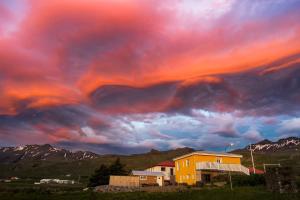 a cloudy sky with a yellow house and mountains at Bjarg Apartments in Grundarfjordur +5 photos