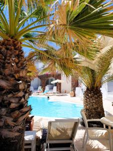 a swimming pool with two palm trees and chairs at Arion Bay Hotel Santorini in Kamari