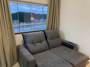 a couch in a living room with a large window at Apartamento Paraíso da Ilha Porchat ! *Novíssimo!* in São Vicente