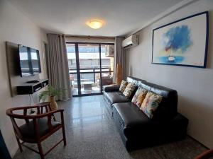 a living room with a black leather couch and a television at Flat Atlântico Meireles by Escala in Fortaleza