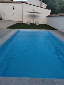 a blue swimming pool with an umbrella and chairs at La Noguera Casa Rural in Huéscar