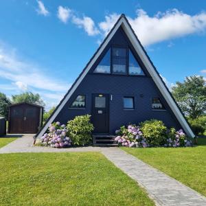 a black house with a pointed roof with flowers at Nurdachhaus PIRATENWEG 131 in Butjadingen