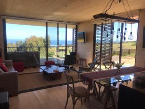 a living room with a table and chairs and large windows at CÓMODA CASA FAMILIAR Punta Lobos in Pichilemu
