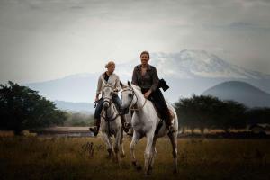 two people riding on horses in a field at Raha Wildlife Resort in Arusha