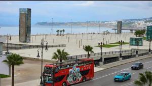 een rode bus die over een weg langs een strand rijdt bij Appart malabata in Tanger