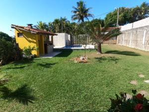 a yard with a yellow house and a fence at Casa de Temporada Meaipe in Guarapari