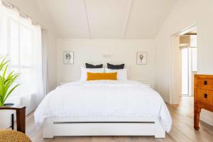 a white bedroom with a white bed with an orange pillow at Spacious, Breezy Studio Apartment, Moments from Downtown and Beach in Mount Maunganui