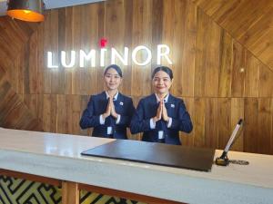 two women in uniform praying in front of a wall at Luminor Hotel Jemursari By WH in Surabaya