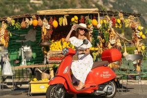 a woman riding a red scooter in front of a fruit stand at Il Barilotto in Positano