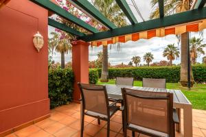 a patio with a table and chairs and palm trees at Hoyo I by Ĥ - Isla Canela Golf GHHI16B2P75 in Isla Canela