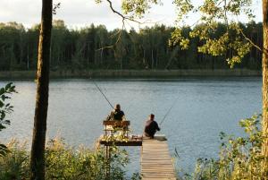 two men sitting on a dock fishing on a lake at Ośrodek Wypoczynkowy Zacisze in Śliwice