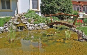 a pond with a bridge in a garden at Hotel Prezident in Palić