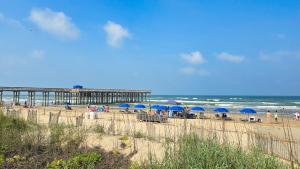 a beach with blue umbrellas and a pier at Seagulls Serenade Cozy 1BR Hideaway near Beach 206 in South Padre Island