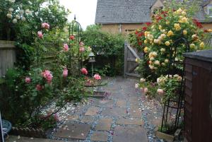 a garden with roses and a gate and a stone pathway at Rose Cottage, Chipping Campden in Chipping Campden