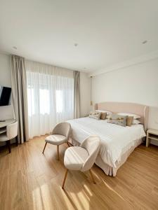 a white bedroom with a large bed and a chair at Feel Boutique Rooms in Oristano