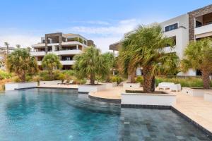 a swimming pool with palm trees in front of a building at The Shore 2 luxury beach front condo in Willemstad