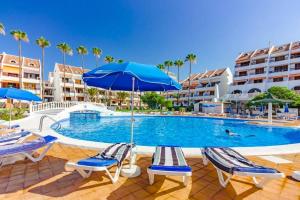 ein Pool mit Stühlen und einem Sonnenschirm sowie einige Gebäude in der Unterkunft Oceanfront Apartment Parque Santiago II in Playa de las Americas