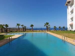 a large blue swimming pool with palm trees and the ocean at Marina Golf location Appartement Climatisé Wifi Piscines Parking Gratuit in Asilah