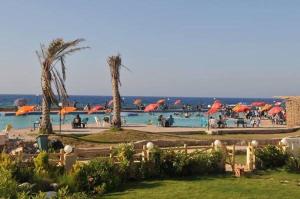a swimming pool with people and umbrellas and the ocean at فيلا ترى البحر بقرية أندلسية مطروح بالتكييفات in Marsa Matruh