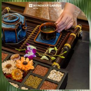 a person holding a cup of tea on a table with food at Wyndham Garden Hoi An Cua Dai Beach in Hoi An