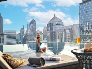 a woman sitting on the edge of a building overlooking a city at Sindhorn Midtown Hotel Bangkok, Vignette Collection by IHG in Bangkok