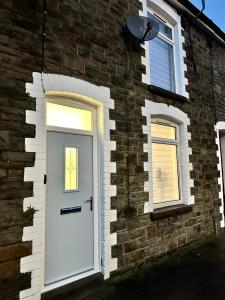 Casa de ladrillo con puerta blanca y 2 ventanas en Stylish Miners Cottage, Treorchy, Rhondda, en Treorky