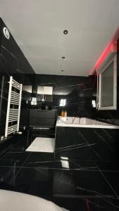 Baño de azulejos negros con bañera y lavamanos en Black Room: Votre Love Room près de Lyon, en Vénissieux