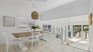 una sala da pranzo bianca con tavolo in legno e sedie bianche di Fairways Beach House - Pool, Golf, Sawtell Village, Family Friendly a Sawtell