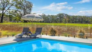 an outdoor swimming pool with two chairs and an umbrella at Koala Lane - Family, Pool, Sleeps 10, Luxe in Bonville