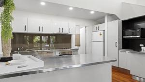 a kitchen with white cabinets and a white refrigerator at Kasuari - Just Steps to Pool and Beach in Coffs Harbour