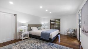 a white bedroom with a bed and a chair at Victoria's - Hamptons Beachside Residence in Emerald Beach
