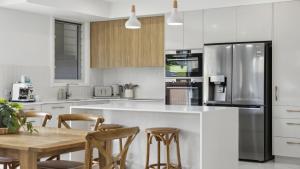 a white kitchen with a wooden table and chairs at Seas the Day - Modern Townhouse in Sawtell Village in Sawtell
