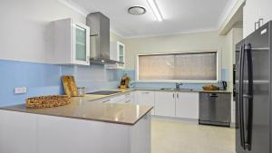eine Küche mit weißen Schränken und einem Edelstahlkühlschrank in der Unterkunft Sea Pine Cottage - In the heart of Sawtell Village, Sleeps 6 in Sawtell + 9 Fotos