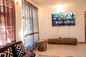 a living room with a table and a tv on the wall at Karibu Nyumbani Hostel in Sokon