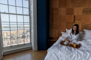 a woman laying in bed with a tray with a teddy bear at Drakes Hotel in Brighton & Hove